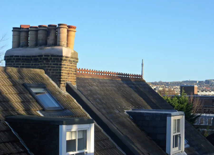 Brick chimney stack with clay pots above slate roofs and dormer windows in Preston Park, Brighton
